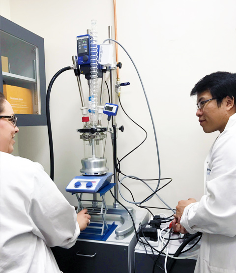 Case studies - Asynt customers share their projects, unique requirements and more. Image shows two chemists with a jacketed lab reactor and a unique DrySyn heating well.